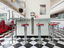 A vintage diner has black-and-white checkered flooring, red vinyl booths, chrome bar stools, and globe pendant lights.