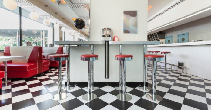 A vintage diner has black-and-white checkered flooring, red vinyl booths, chrome bar stools, and globe pendant lights.